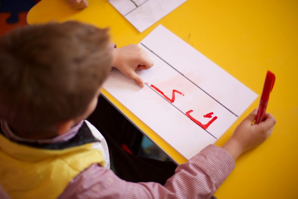 A young child practicing Arabic script writing at school on a bright yellow desk.