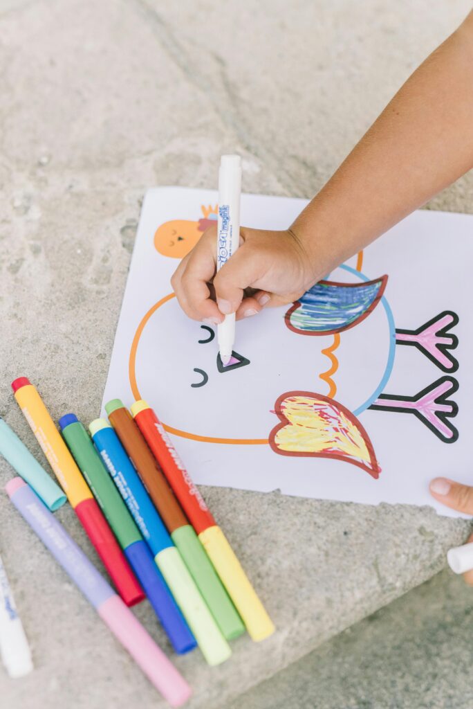 A child coloring a vibrant bird drawing with colorful markers on paper.